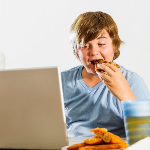 overweight child eating pizza whie looking at a laptop